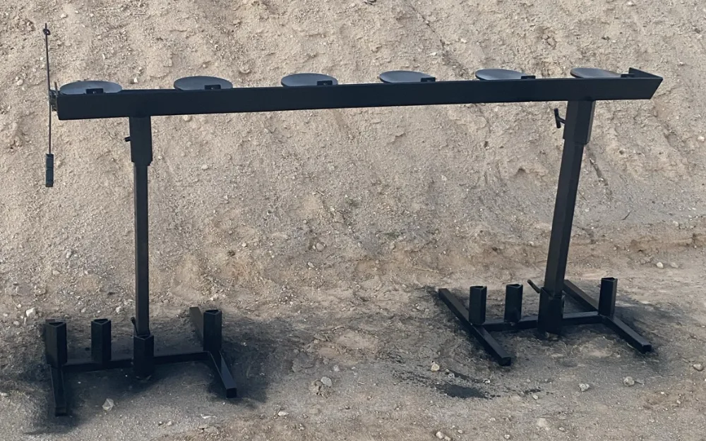 The finished plate rack straight on: six round steel paddles lying along a long bar on two stands, in front of a range berm